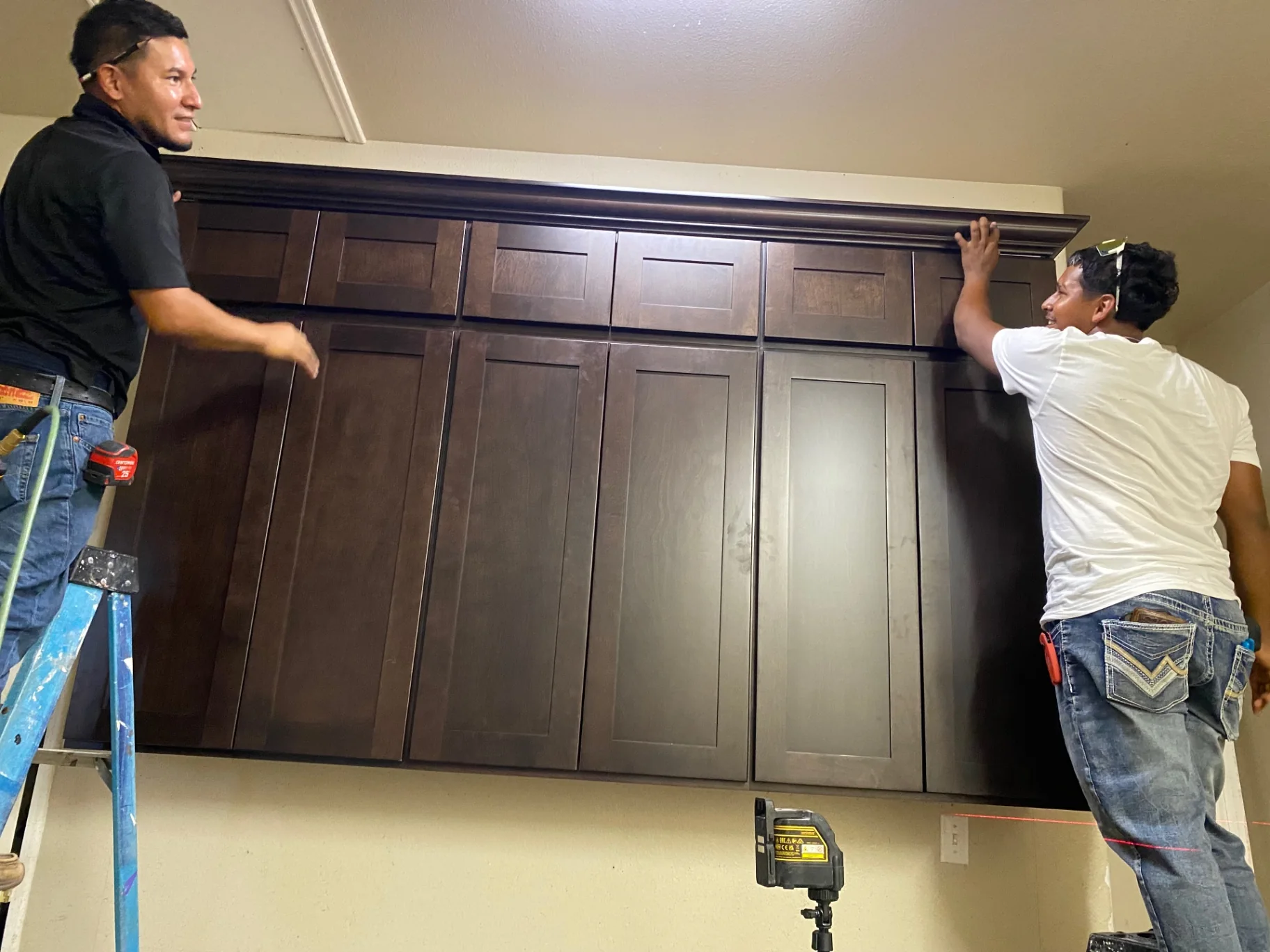 Craftsmen mounting dark upper cabinets during installation
